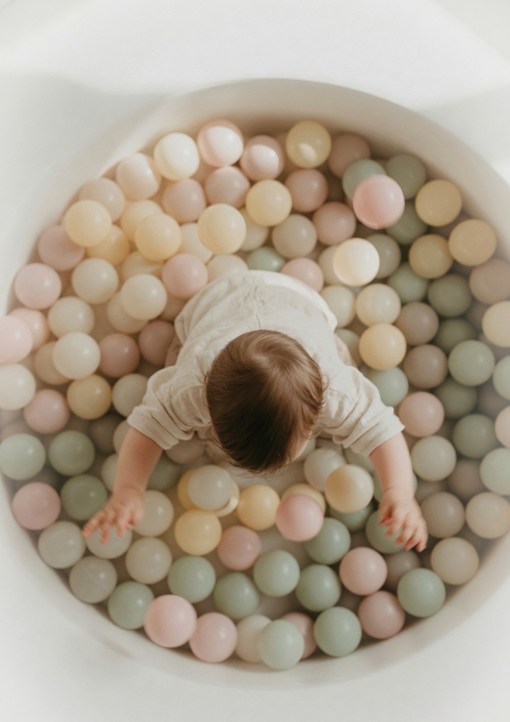 A child playing in a warm pastel ball pit, viewed from above